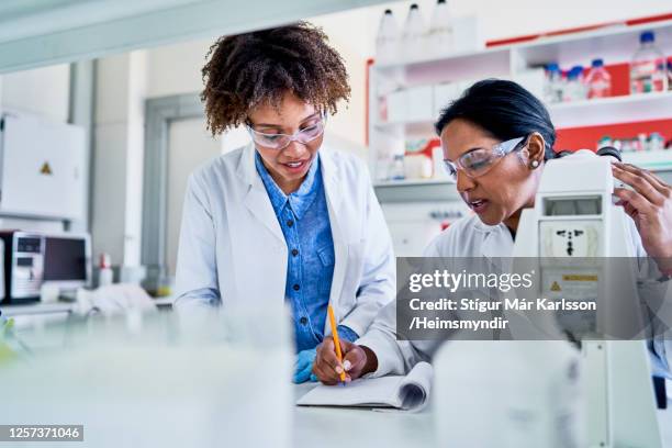 two scientists standing in a lab and writing data in a notebook - scientist standing next to table stock pictures, royalty-free photos & images