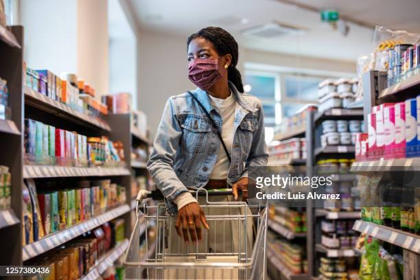 female customer with face mask shopping at a grocery store - fare spese foto e immagini stock