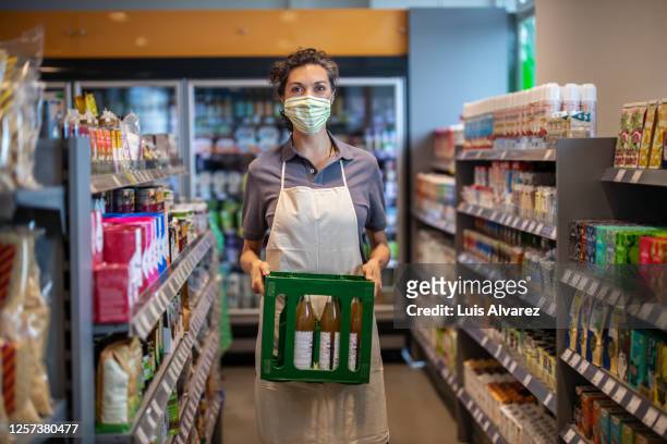 woman with face mask working in a grocery store - essenzielle berufe und dienstleistungen stock-fotos und bilder