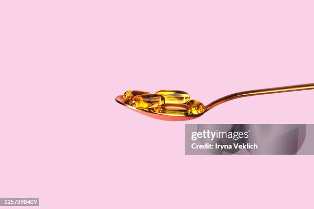 fish oil capsules with omega 3, vitamin d in a spoon on pink background. - vitamins and minerals stock pictures, royalty-free photos & images