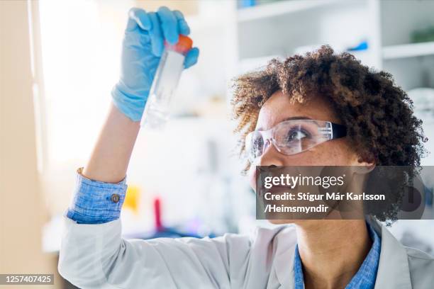 smiling young scientist holding up a research sample in a lab - dna smiley stock pictures, royalty-free photos & images