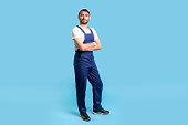 Full length confident professional handyman in overalls standing with crossed hands, smiling at camera