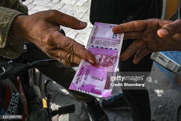 Customer hands a 2,000 rupee banknote to an attendant at a petrol station in New Delhi, India, on Tuesday, May 23, 2023. India withdrawing its...
