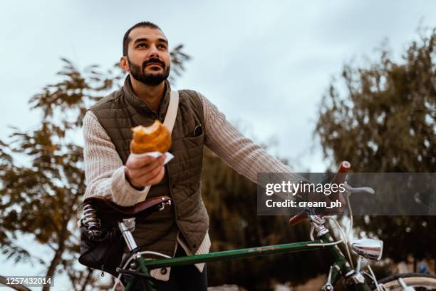 young man with a bicycle eating breakfast in the park - eating on the move stock pictures, royalty-free photos & images