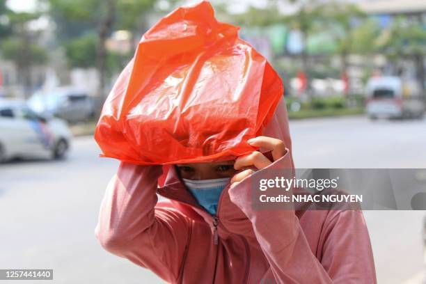 This photo taken on May 22, 2023 shows a woman using a plastic bag to shield herself from the sun while walking on a street of Hanoi.