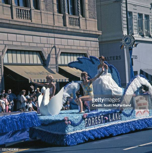 Miss Forest Lake Sandee Marier , wearing an evening gown and elbow gloves, rides on a parade float between her princesses, Sandie Waldo and Sandy...