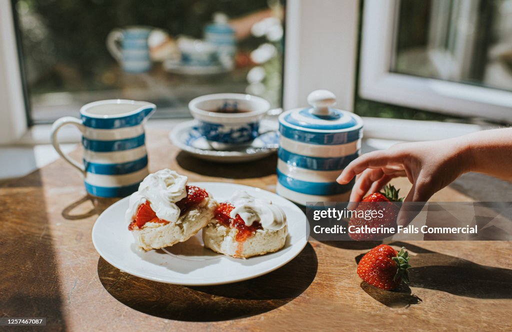 Traditional Afternoon Tea of Scones with Jam and Clotted Cream - Child grabs a strawberry