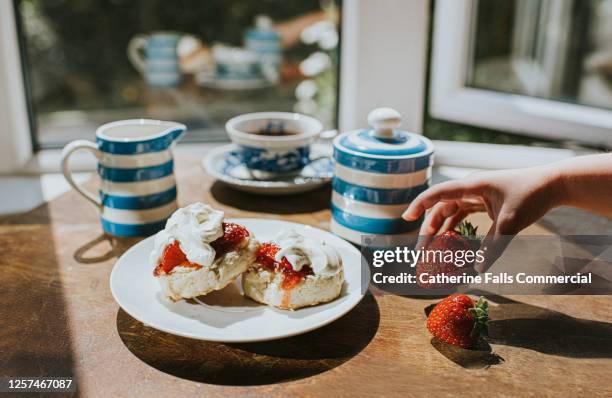 traditional afternoon tea of scones with jam and clotted cream - child grabs a strawberry - scone stock pictures, royalty-free photos & images