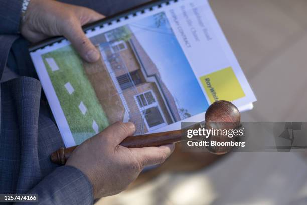 An auctioneer holds a home pamphlet and gavel in an arranged photograph after an auction of a property in Sydney, Australia, on May 20, 2023. In...