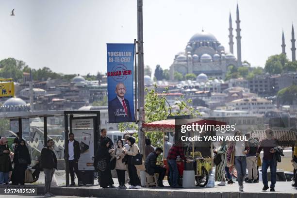 People shop and wait at a bus stop next to a campaign poster of the leader of the Republican People's Party and presidential candidate of the Nation...