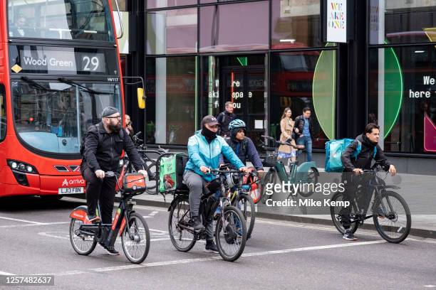 Cyclists and food delivery cycle couriers wait at the lights ahead of a bus on 22nd May 2023 in London, United Kingdom. Cycling is a very popular...