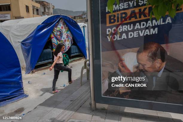 Woman walks past humanitarian tents and an election poster for Turkish President Recep Erdogan in Hatay, on May 22 one of the cities worst affected...