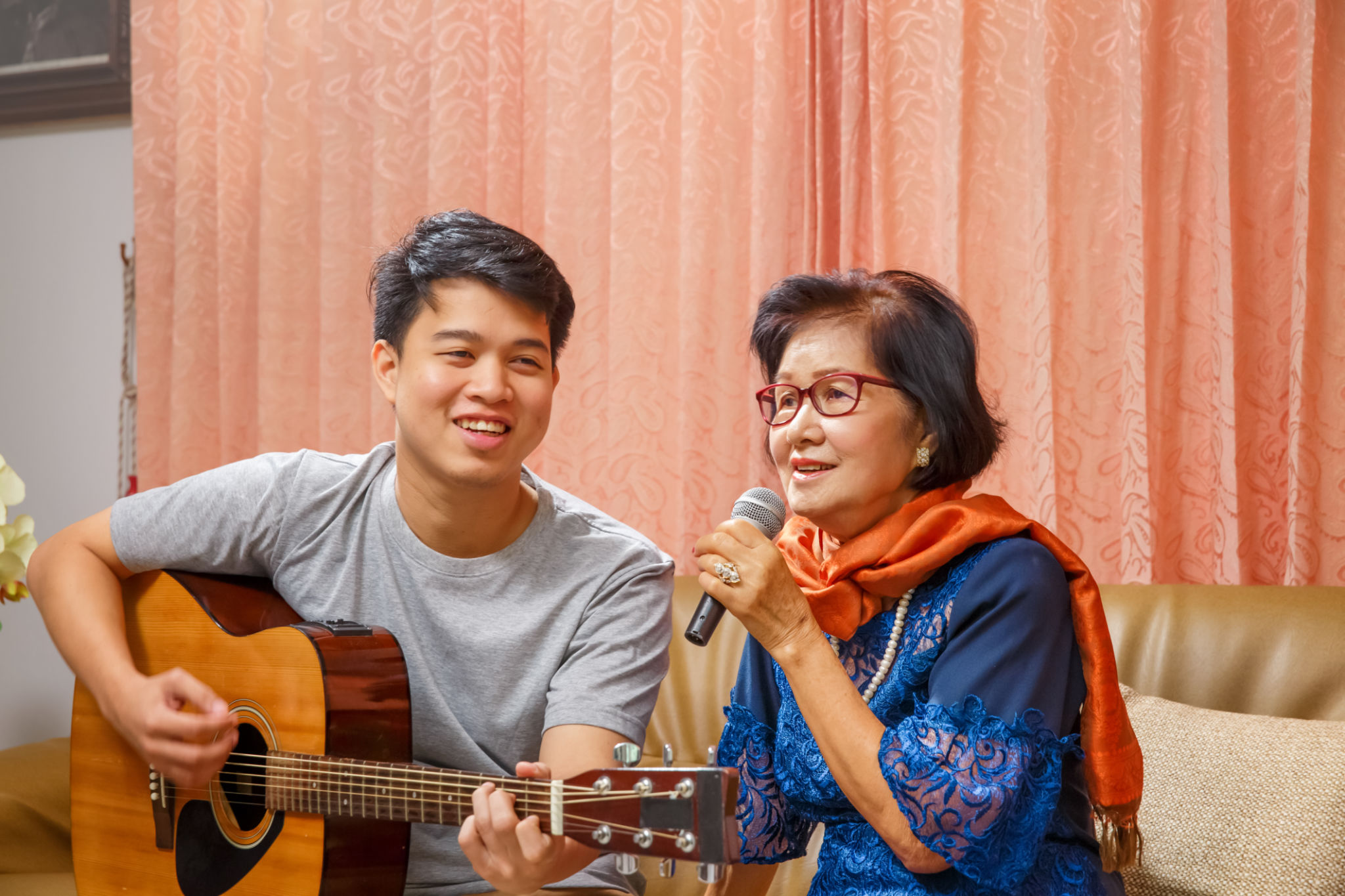 Adult son and senior mom sing a song while relaxed sitting on couch Adult son and senior mom sing a song while relaxed sitting on couch