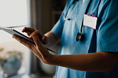 Close-up of female doctor in scrubs with digital tablet, typing and completing checklist