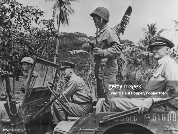 Lieutenant General Holland Smith of the United States Marine Corps stands up in a jeep to pick out points of interest to his visitors, in front seat...