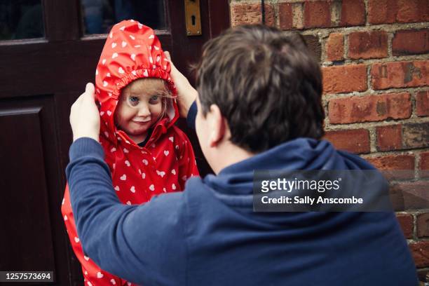 little girl getting ready to go outside to walk to school - regenmantel stock-fotos und bilder