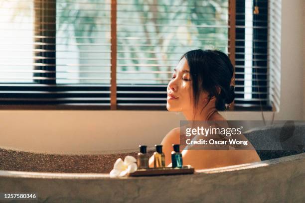 staycation: young happy woman enjoying in bubble bath in hotel bathroom with her eyes closed - taking a bath stock pictures, royalty-free photos & images