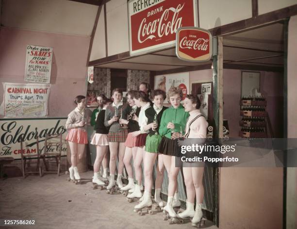 Group of young female roller skaters stand at a counter and drink from bottles of Coca-Cola at a cafe attached to a roller skating rink in Norwich,...