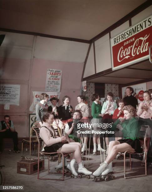 Group of young female roller skaters drink from bottles of Coca-Cola at a cafe attached to a roller skating rink in Norwich, Norfolk, England in May...