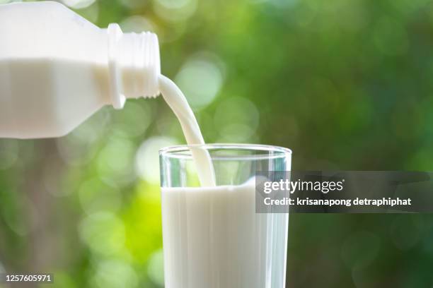 woman hand holding bottle with fresh milk pouring into glass on wooden table,milk - milk pour - fotografias e filmes do acervo