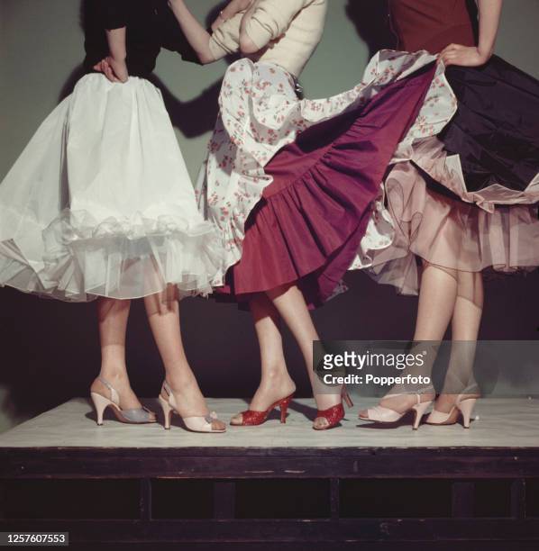 Half length studio image of three women wearing red, pink and white petticoats, underskirts and waist slips as fashionable party skirts, England, May...