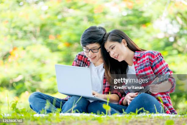 couple lgbt women sit in park or garden with one use tablet and the other play ukulele or small guitar with morning light - asian lesbians kiss stock pictures, royalty-free photos & images