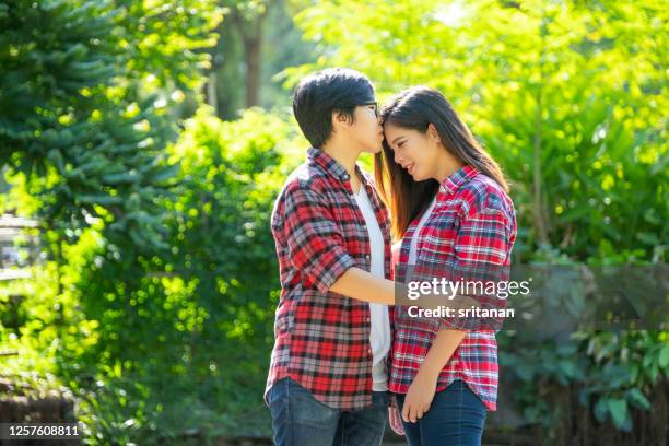 couple lgbt women stand closely together then one kiss on one forehead in garden - asian lesbians kiss stock pictures, royalty-free photos & images