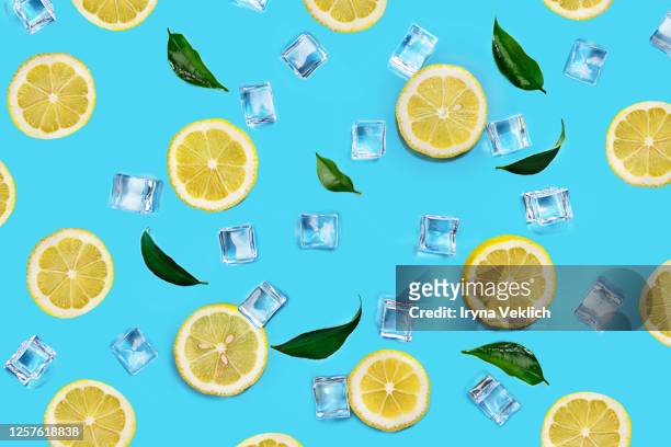tropical abstract pattern with lemon fruits, ice cubes and green leaves on blue color background. - mint green fotografías e imágenes de stock