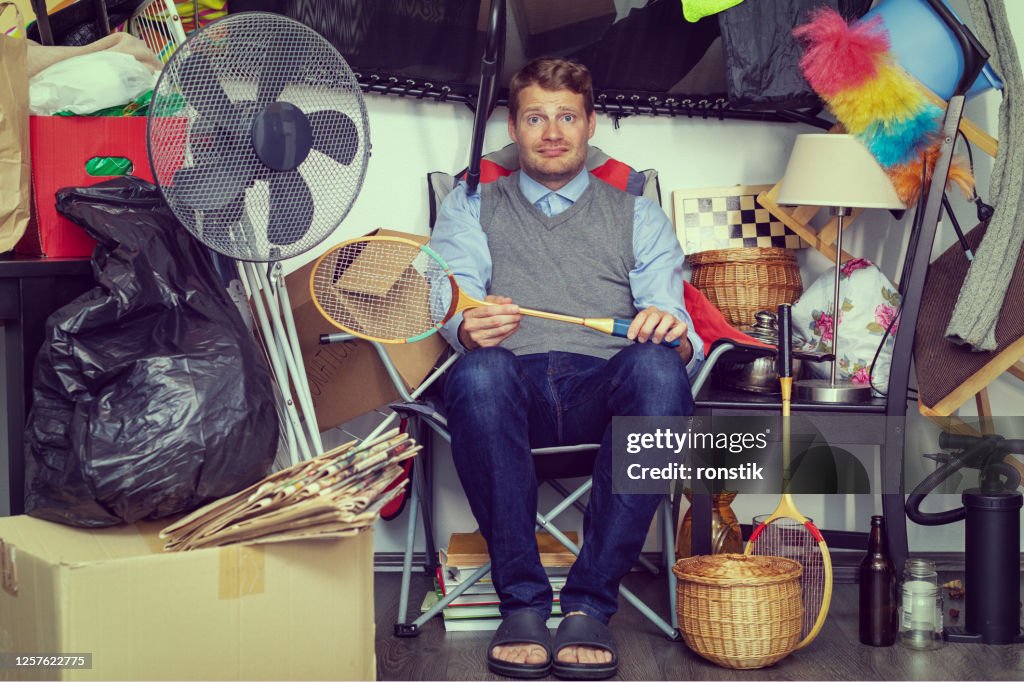 Compulsive hoarding disorder concept - man hoarder with stuff piles sitting in the room