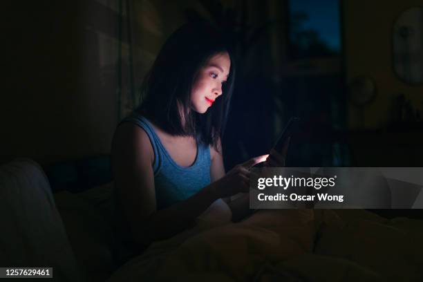 young woman looking at smart phone before bed - surfing the net stock pictures, royalty-free photos & images