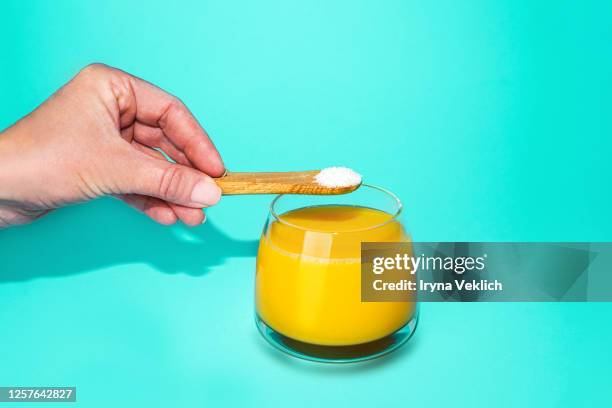 hand with spoon of protein or collagen and orange juice on mint green color background. - sistema immunitario foto e immagini stock