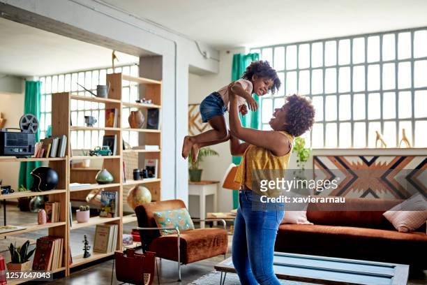 afro-caribbean mother and young daughter playing at home - picking up child stock pictures, royalty-free photos & images