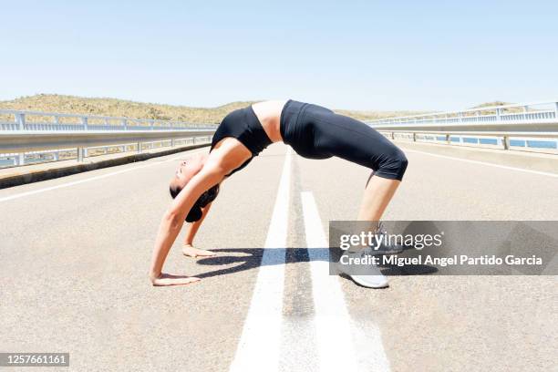 young sportsman practicing yoga, doing bridge exercise on the city road - archive photo - yoga caliente fotografías e imágenes de stock