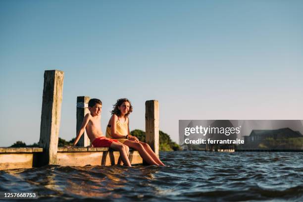 siblings dipping feet in water on pier - outer banks stock pictures, royalty-free photos & images