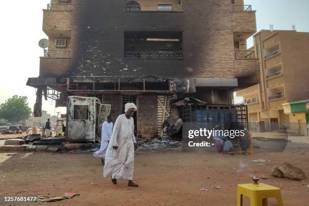 Men walk past others sitting outside a burnt-down bank branch in southern Khartoum on May 24, 2023. Sporadic artillery fire still echoed in Sudan's...