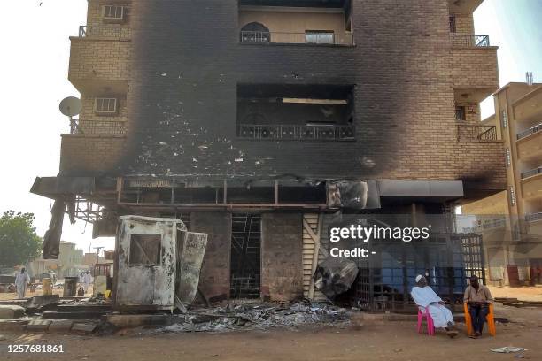 Men sit outside a burnt-down bank branch in southern Khartoum on May 24, 2023. Sporadic artillery fire still echoed in Sudan's capital on May 24 but...