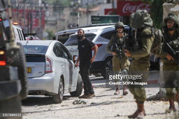 An Israeli settler checks a car belonging to another settler, after it was pelted with stones, in the town of Hawara, south of Nablus, in the...