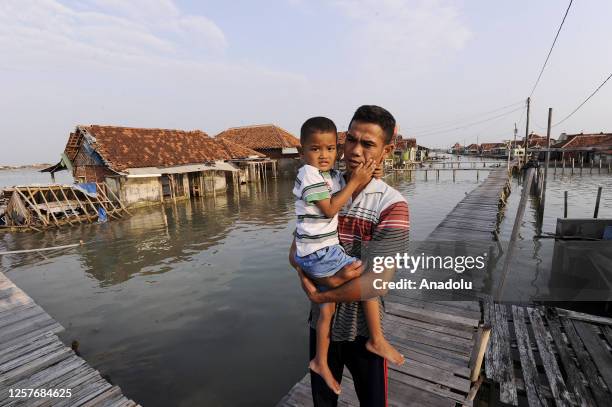 Man and his child pose for a photo on the pier in front of the damaged houses which has been hit by a tidal wave in Demak, Central Java, Indonesia on...