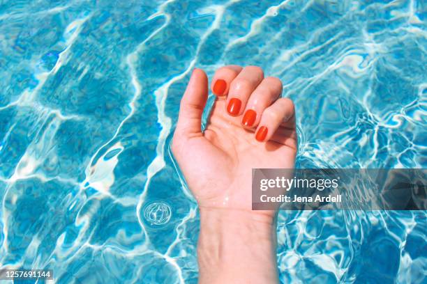 woman's wrist in swimming pool, woman's hand, red nail polish summer fingernails - red nail polish stockfoto's en -beelden