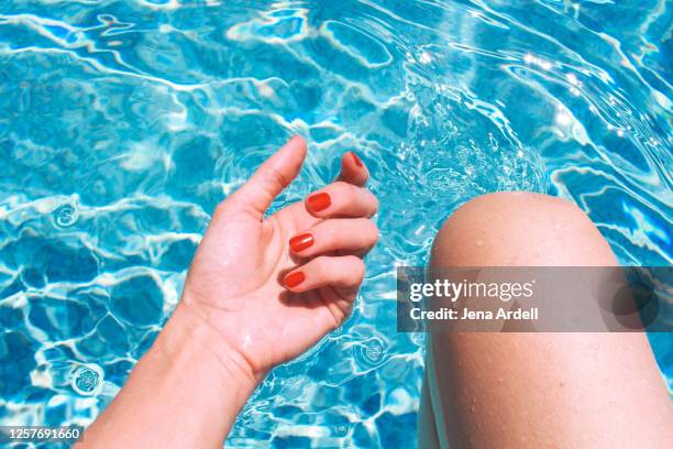 woman's hand and woman's knee in swimming pool, red nail polish on fingernails - fingernail foto e immagini stock