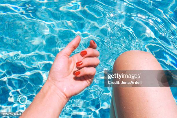 woman's hand and woman's knee in swimming pool, red nail polish on fingernails - hand on knee ストックフォトと画像