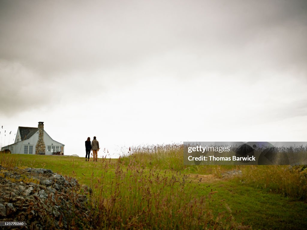 Young couple standing in grass looking at home