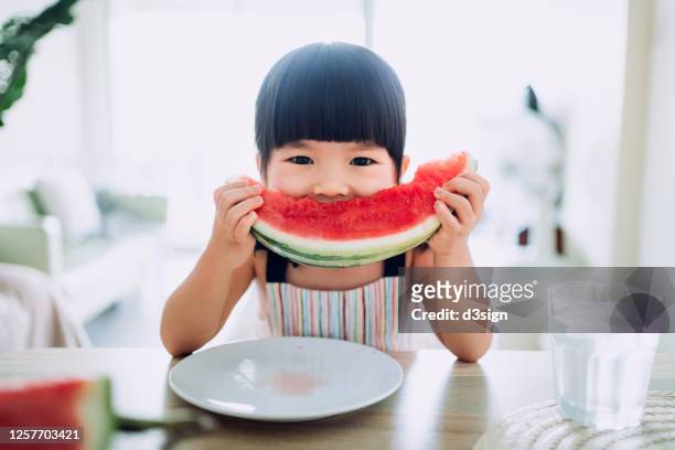 adorable little asian girl eating a slice of watermelon at home - child eating a fruit stockfoto's en -beelden
