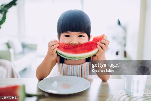 adorable little asian girl eating a slice of watermelon at home - child eating juicy stock pictures, royalty-free photos & images