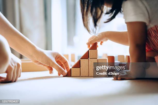 close up of mother and little daughter sitting on the floor playing with wooden building blocks together and enjoying family bonding time at home - home concepts stock-fotos und bilder