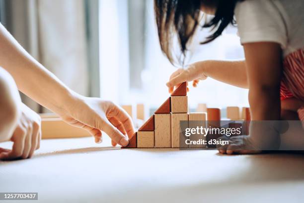 close up of mother and little daughter sitting on the floor playing with wooden building blocks together and enjoying family bonding time at home - vie simple photos et images de collection