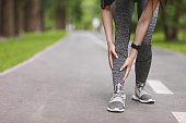 Young female runner suffering from shin splints while jogging in park