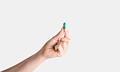 Unrecognizable young girl showing one blue pill over white background, closeup