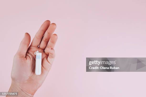 tampon in a female hand on a pink background - tampon stock pictures, royalty-free photos & images