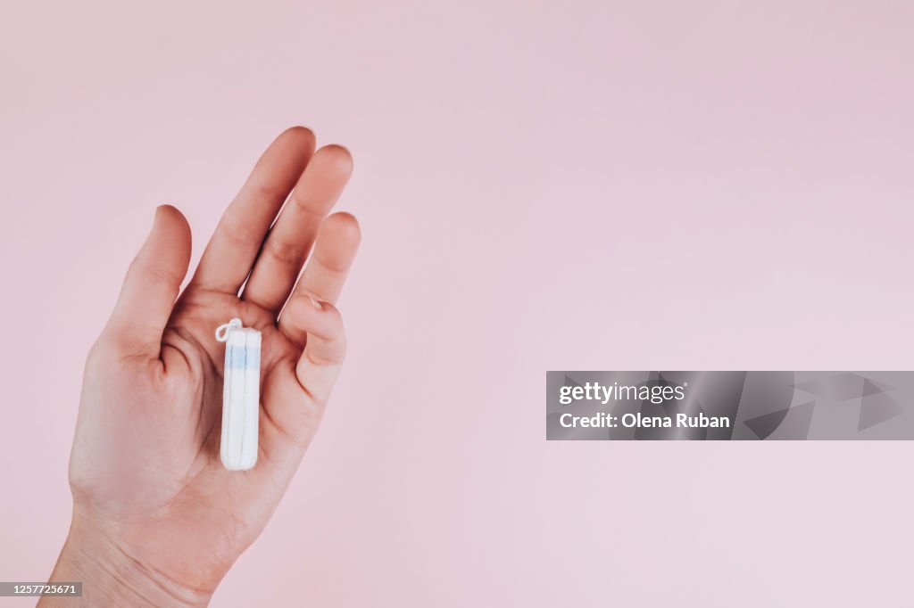 Tampon in a female hand on a pink background